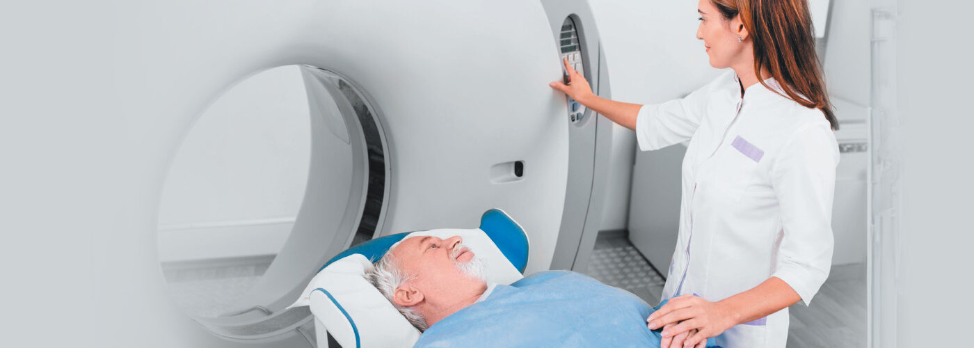 Female nurse holds hand of male patient as he lays on MRI machine