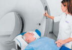 Female nurse holds hand of male patient as he lays on MRI machine