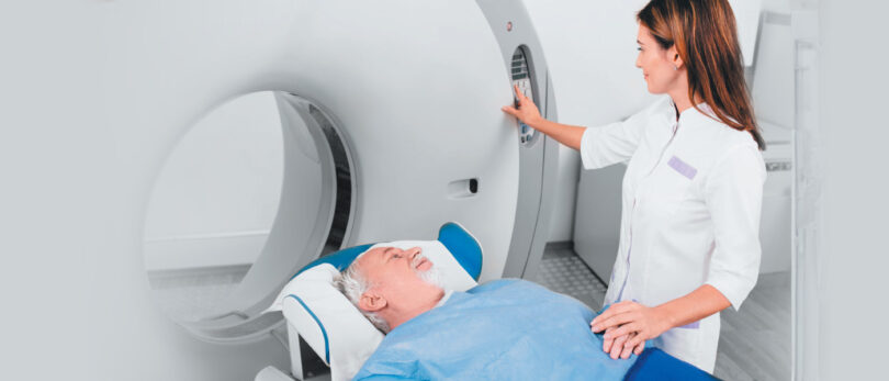 Female nurse holds hand of male patient as he lays on MRI machine