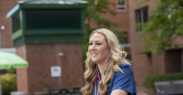 Female nurse in front of a building smiling and staring far off.